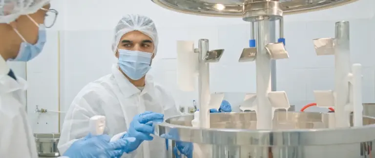 Carmel team in hair caps and masks checking a cream batch at an open stainless steel mixer