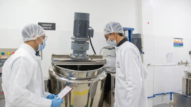 Two Carmel technicians in hair caps checking a batch at a stainless steel mixer, tablet in hand