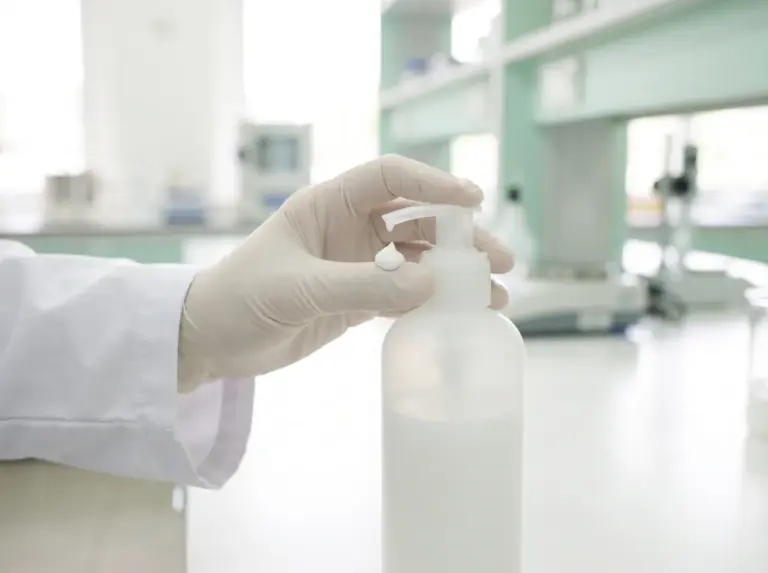 Gloved hand pressing the pump of a white lotion bottle in a laboratory