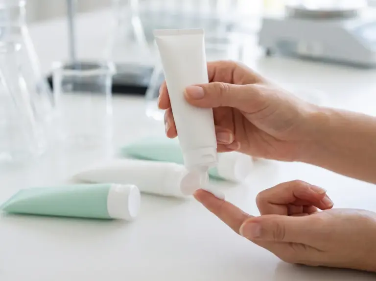 Hands holding a white cosmetic tube above blank tubes in a laboratory