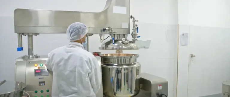 Carmel technician at a large stainless steel vacuum emulsifying mixer in the production room